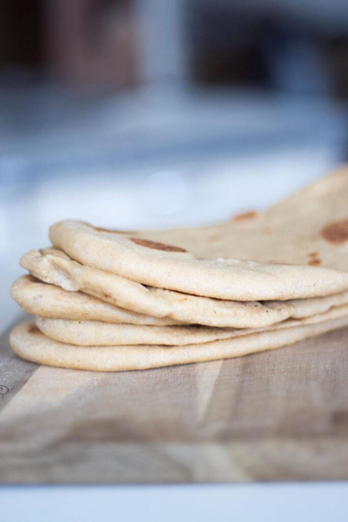 This is a side photo of a stack of flatbread on a wood cutting board.