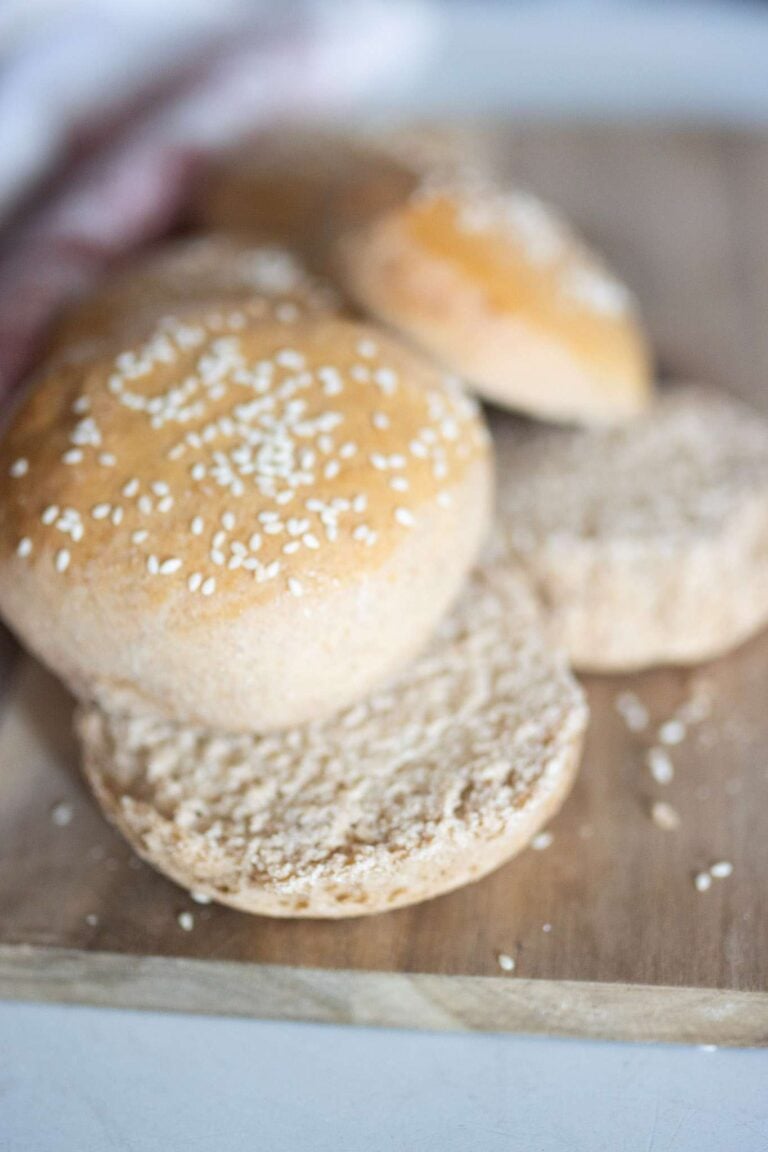 A golden brown fresh milled hamburger bun sits on a cutting board and is sliced open.