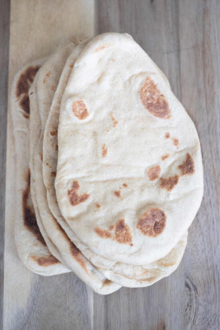 An overhead photo of a stack of flatbread on a wooden cutting board