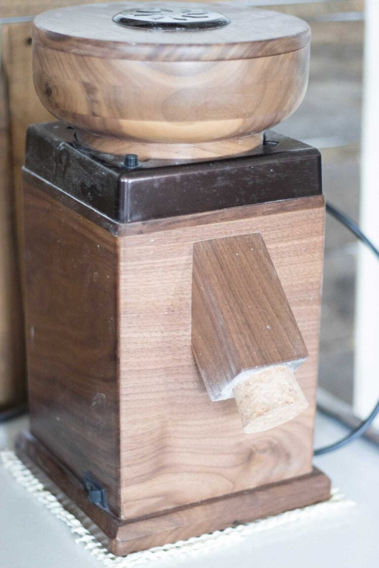This is a dark wood grain mill with a cork in the spout. It is sitting on a white counter.