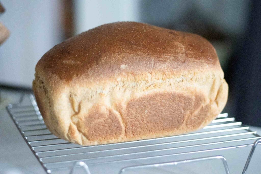 a golden brown loaf of bread sits on a silver cooling rack.
