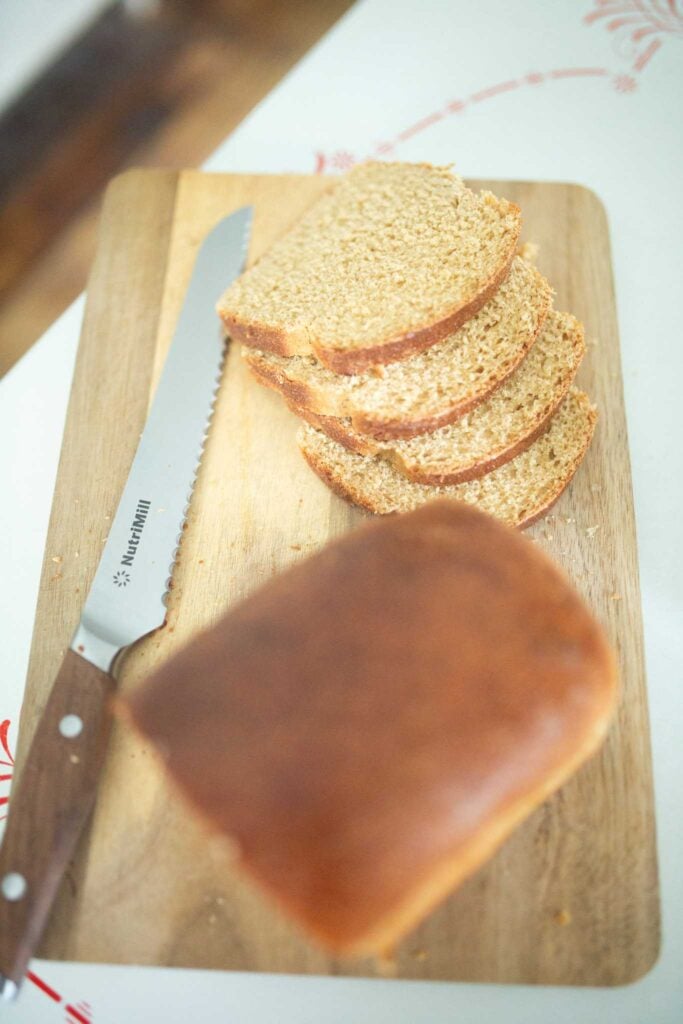 A half loaf of bread sits in front of slices on a cutting board with a bread knife.