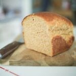 Half a loaf of bread sitting on a cutting board with a bread knife