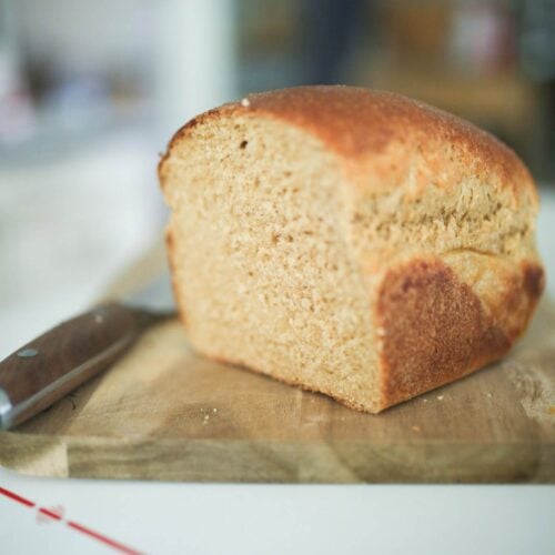 Half a loaf of bread sitting on a cutting board with a bread knife