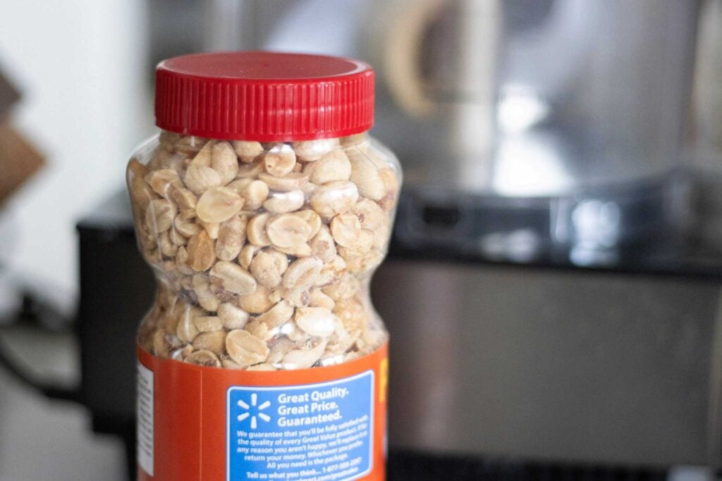 A jar of peanuts sits in front of a food processor