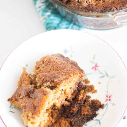 Piece of sourdough coffee cake in white and floral bowl in front of the oval glass baking dish of coffee cake.