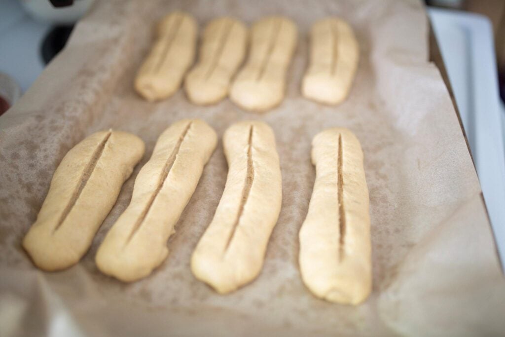 Hoagie sandwich roll dough scored straight down the top before baking on a parchment lined baking sheet.