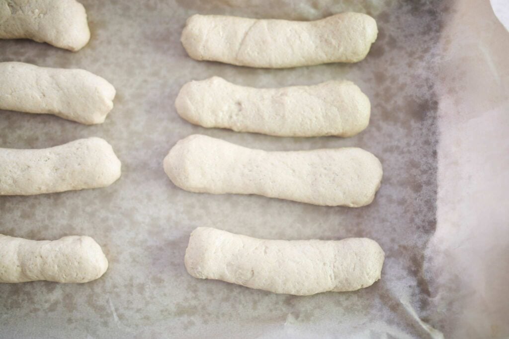 Hoagie shaped dough on a parchment lined baking sheet.