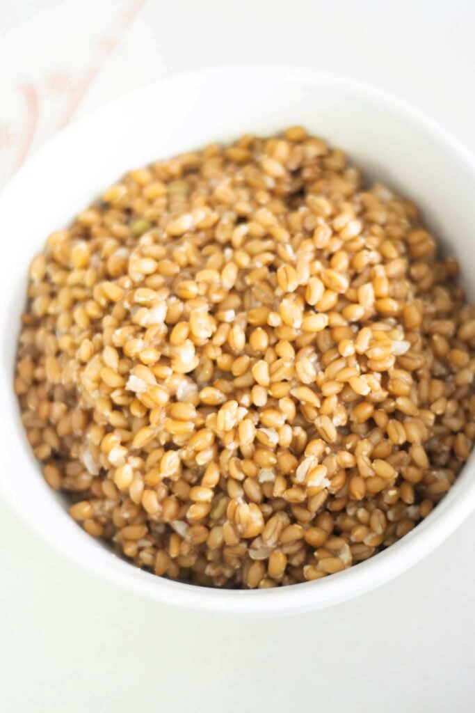 A close, overhead picture of cooked wheat berries in a white bowl on a white table.