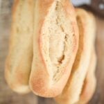 This is an overhead photo of golden brown sandwich rolls stacked on top of each other on a wooden board.