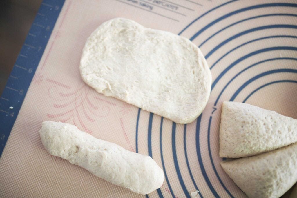 Hoagie roll dough is pressed out into a rectangle while a shaped dough is in the foreground.