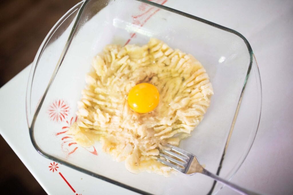 Mashed bananas are topped with an egg in a square glass pan.