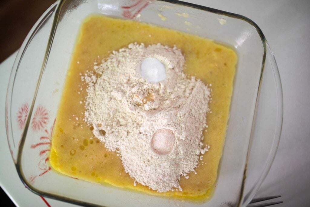 Wet ingredients topped with dry ingredients in a glass square pan.
