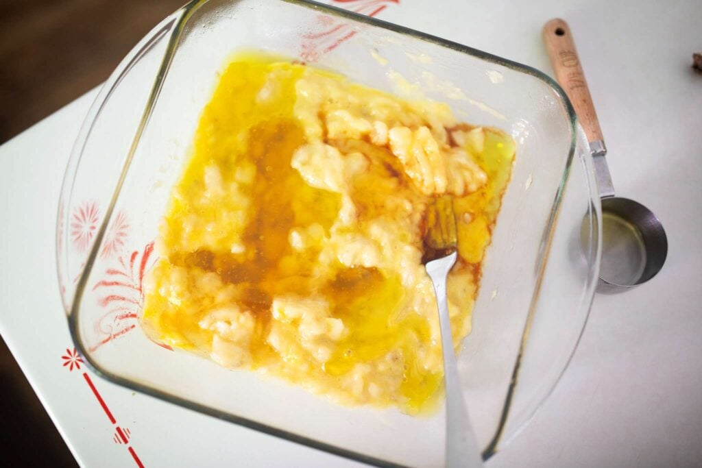 Mashed bananas, oil, and vanilla in a glass square pan.