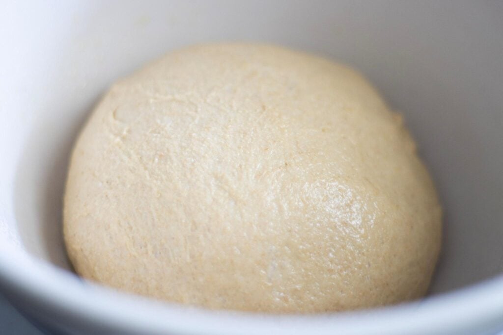 There is a glossy ball of dough in a cream bowl.