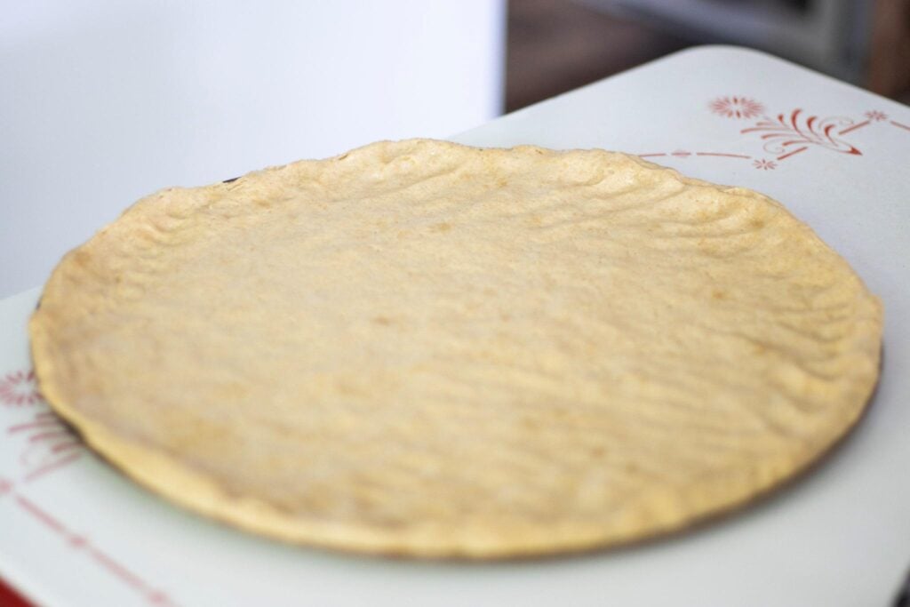 Pizza dough is spread out on a pizza pan sitting on a white table.