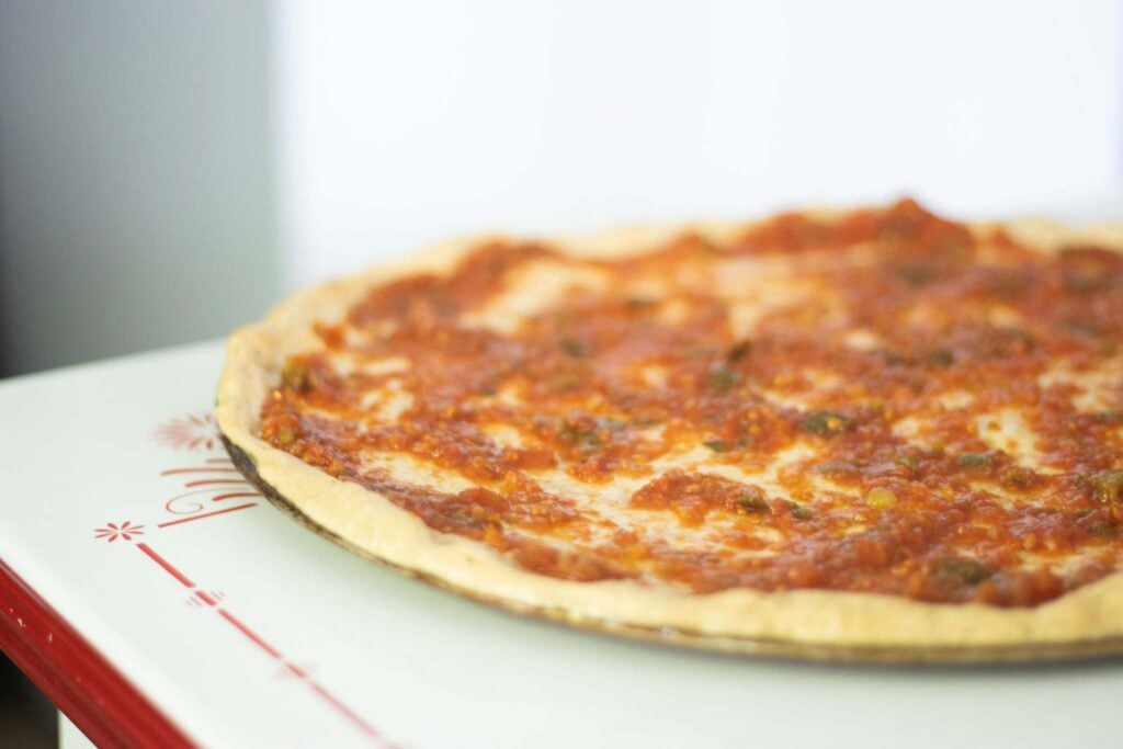 Pizza dough is topped with red sauce.