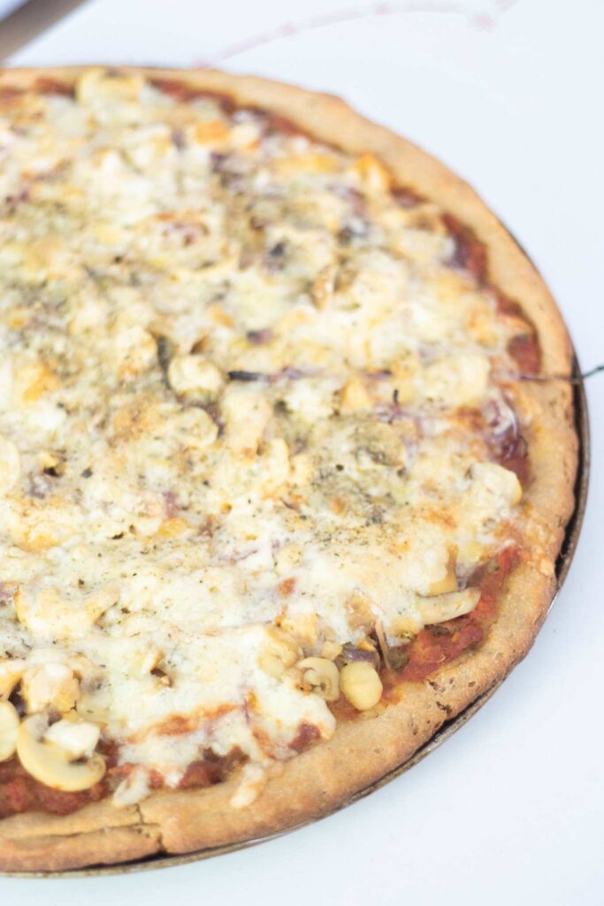 An overhead photo of a pizza on the pizza pan. It is topped with cheese and you can see the red sauce underneath.