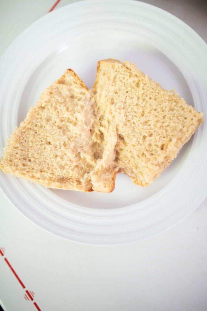 ciabatta bread is cut open to show the light and airy crumb. It sits on a white plate.