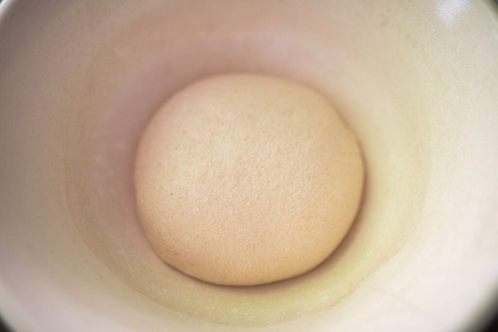 A ball of dough sits in a cream colored bowl.