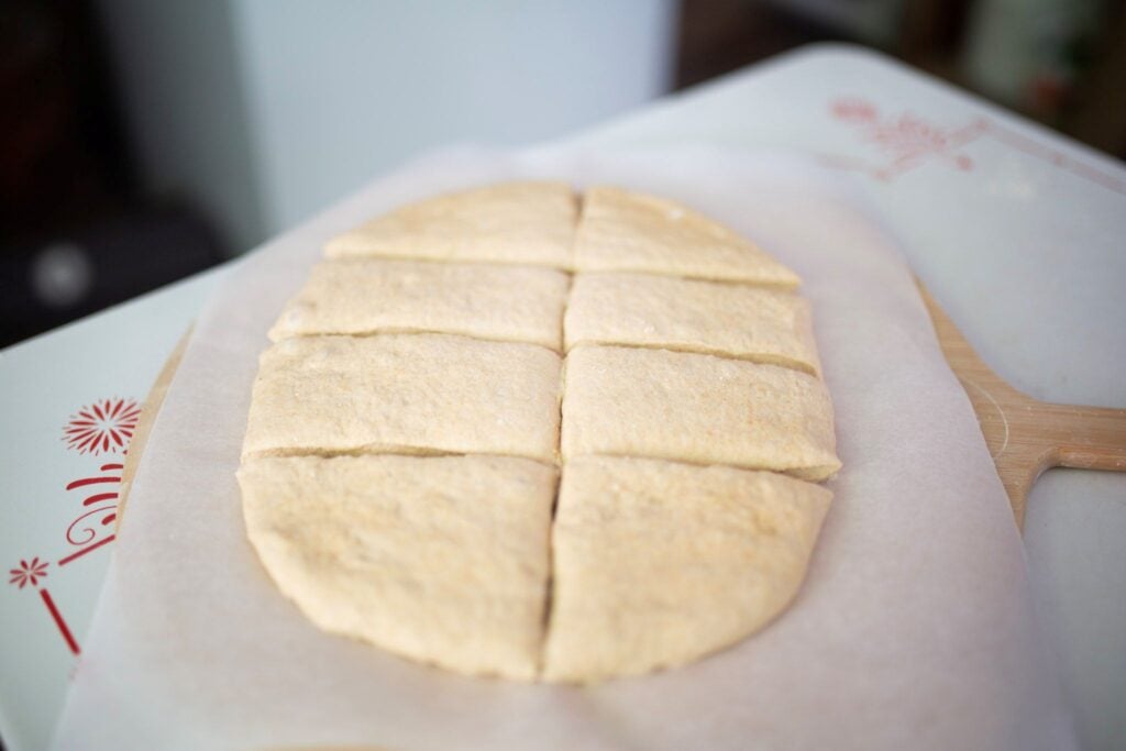 dough is scored into 8 equal pieces on a piece of parchment paper.