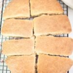 8 pieces of ciabatta bread sit on a black wire rack with a red and white towel in the background.