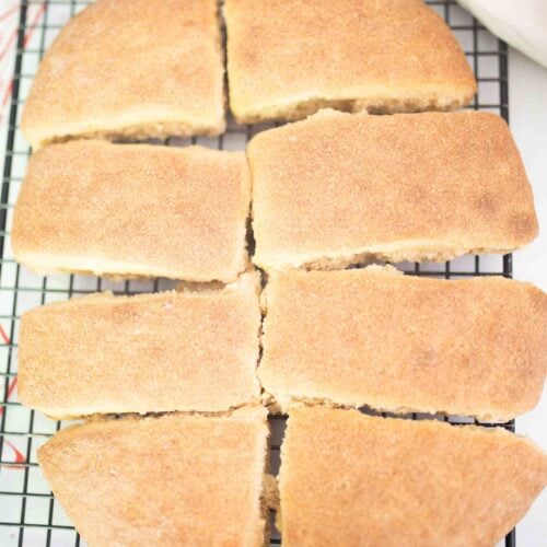 8 pieces of ciabatta bread sit on a black wire rack with a red and white towel in the background.