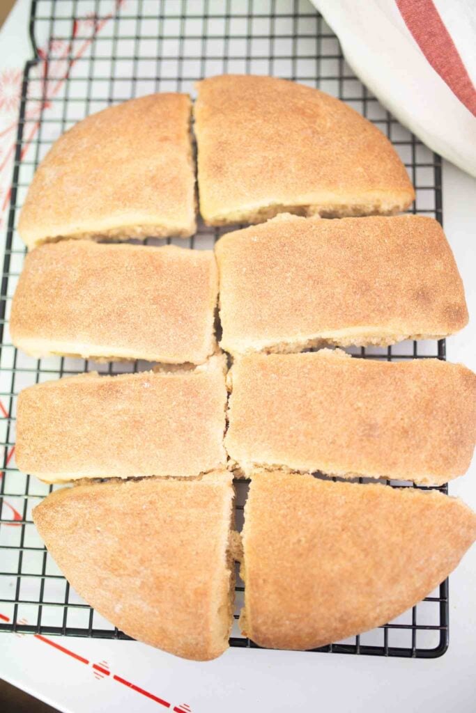 8 pieces of ciabatta bread sit on a black wire rack with a red and white towel in the background.