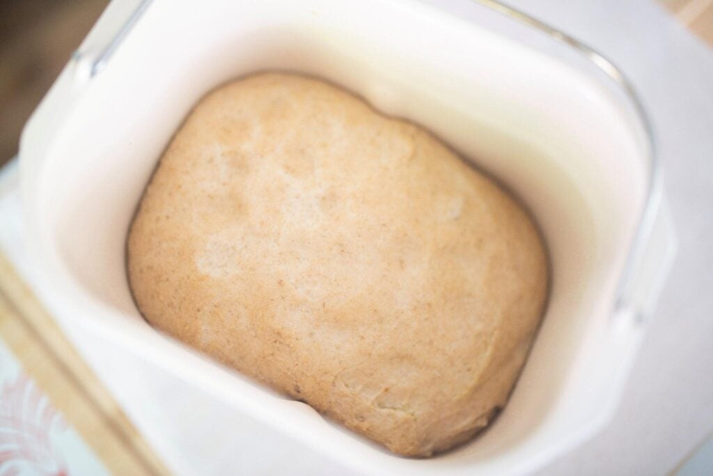 There is dough risen in a bread machine pan sitting on the counter.
