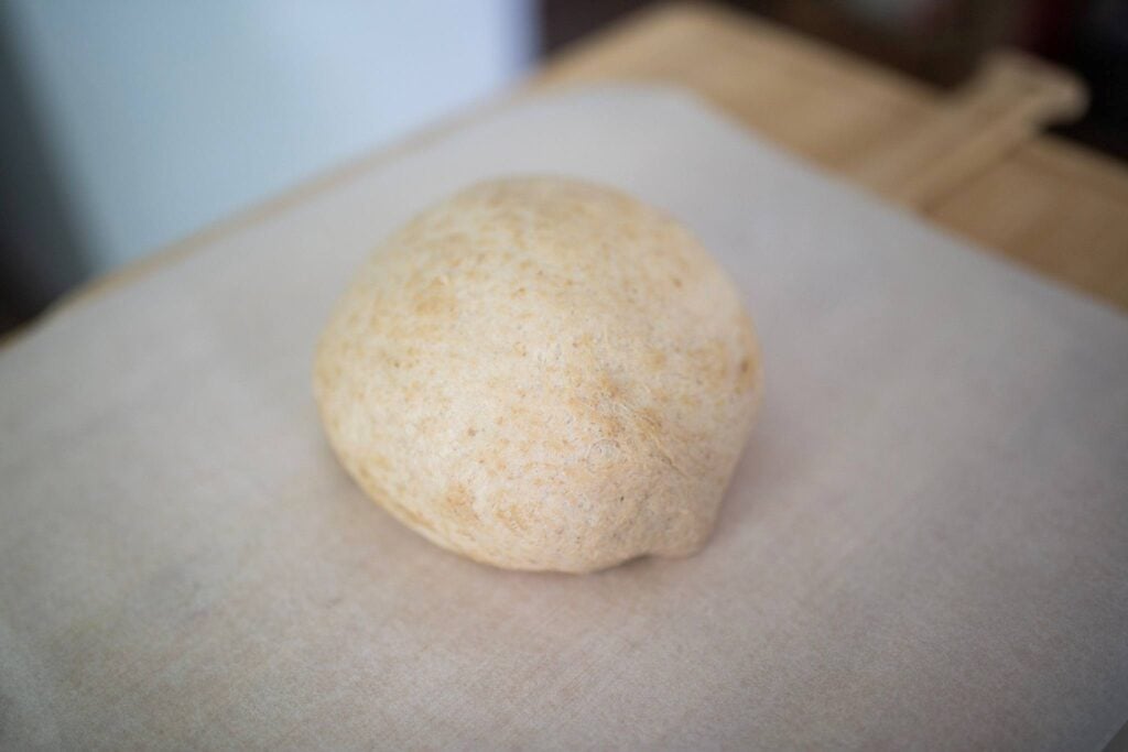 A ball of dough sits on a piece of parchment paper.