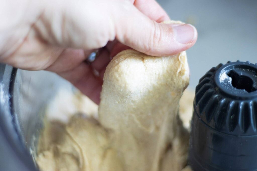 A hand is holding up dough from a mixer that is stretchy.