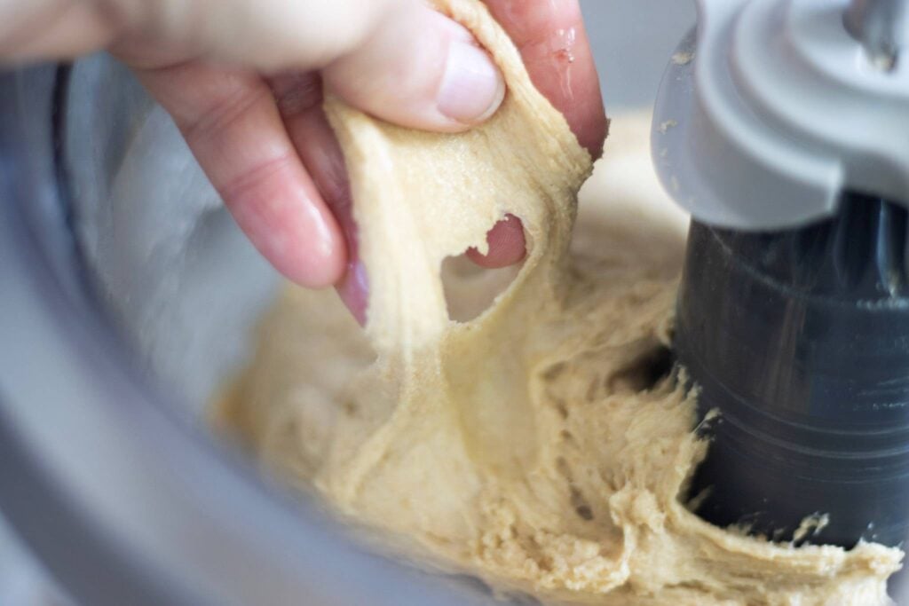 A hand is pulling dough up from a mixing bowl. The dough is broken.