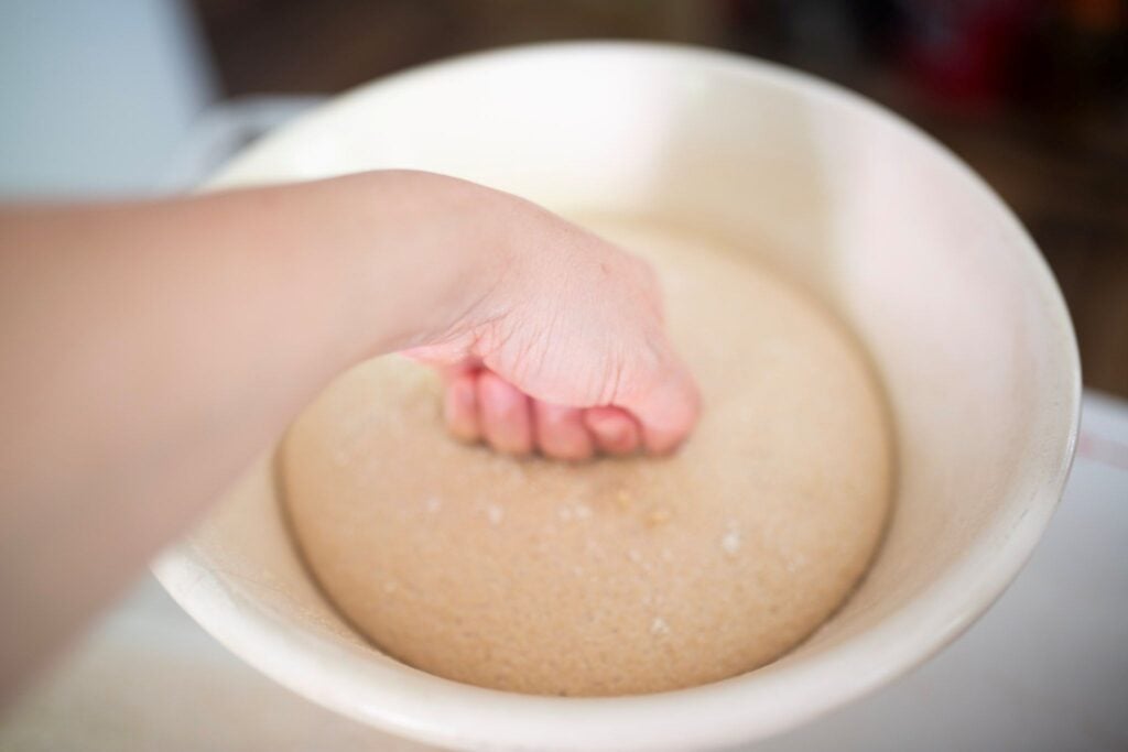 There is a hand punching down a ball of risen dough.