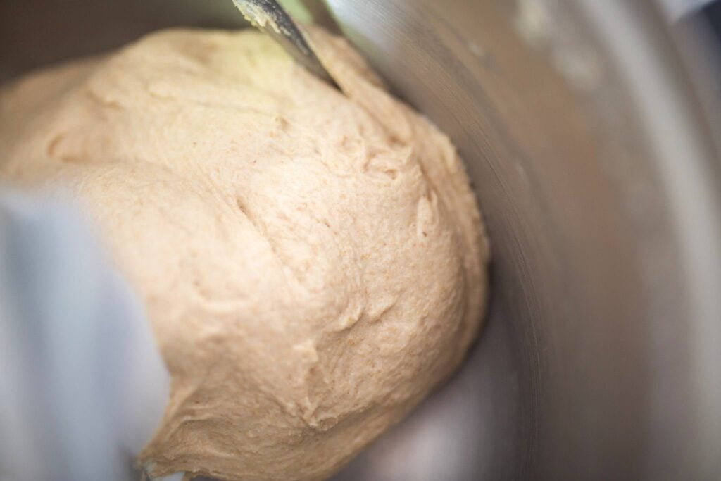 There is a ball of dough that has been kneaded in a stainless steel mixing bowl.