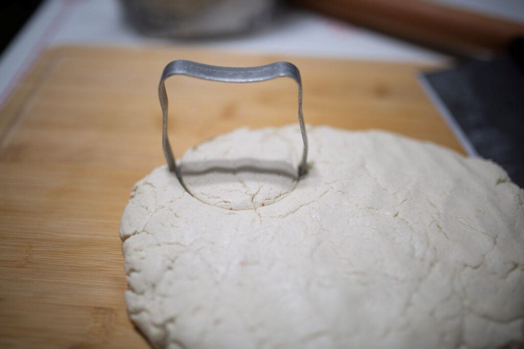 A biscuit cutter cutting into biscuit dough on a cutting board.