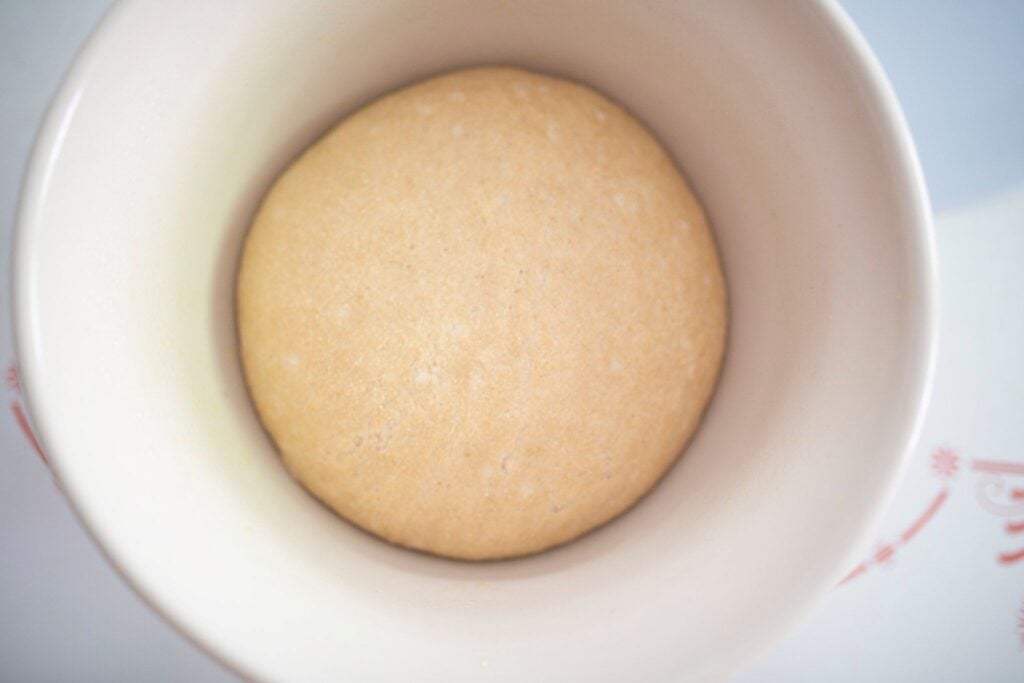Risen dough ball in a cream colored bowl.