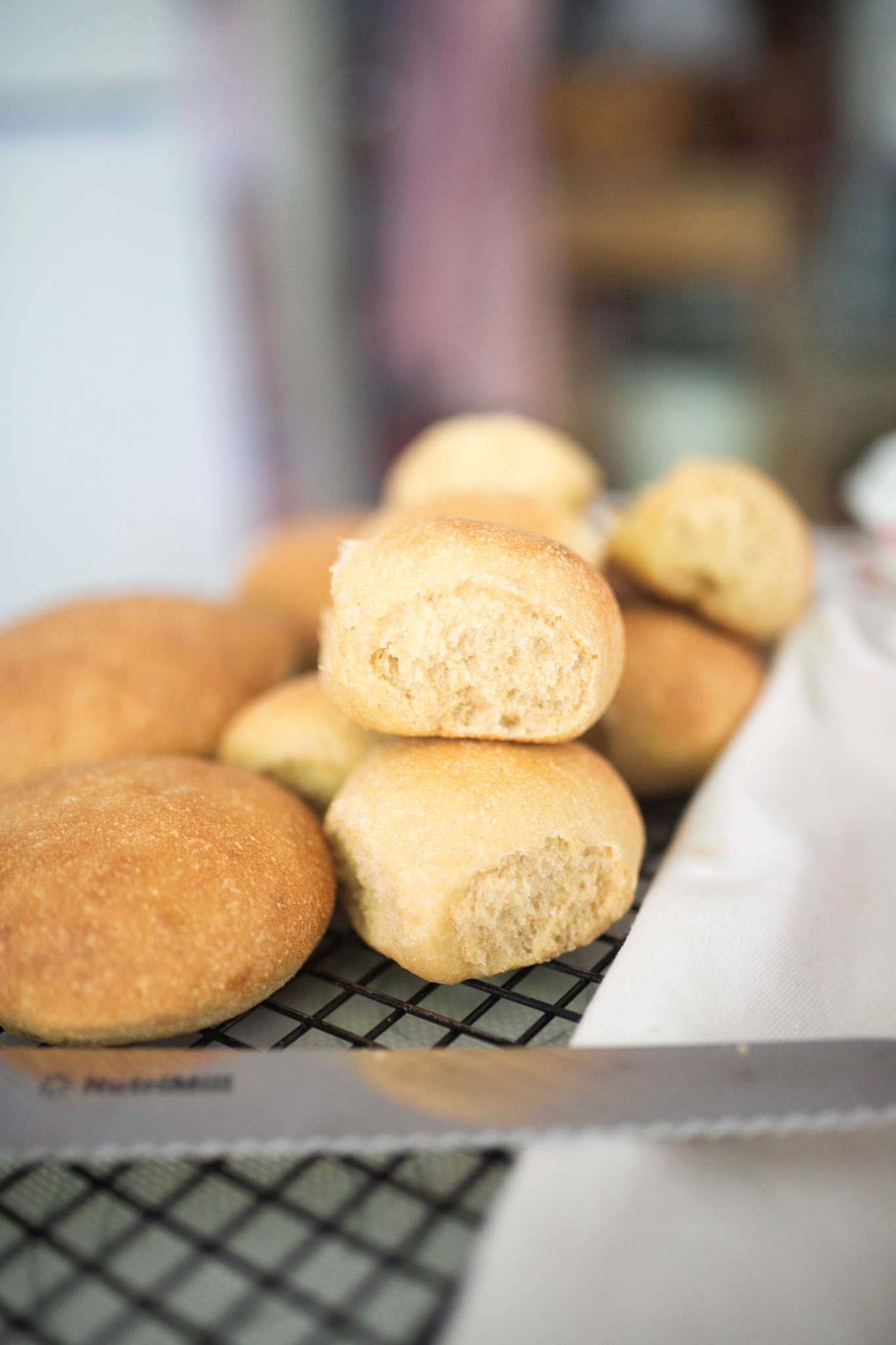 Side view of rolls and buns on a cooling rack with a bread knife. One roll is stacked on top of the others to show the crumb.