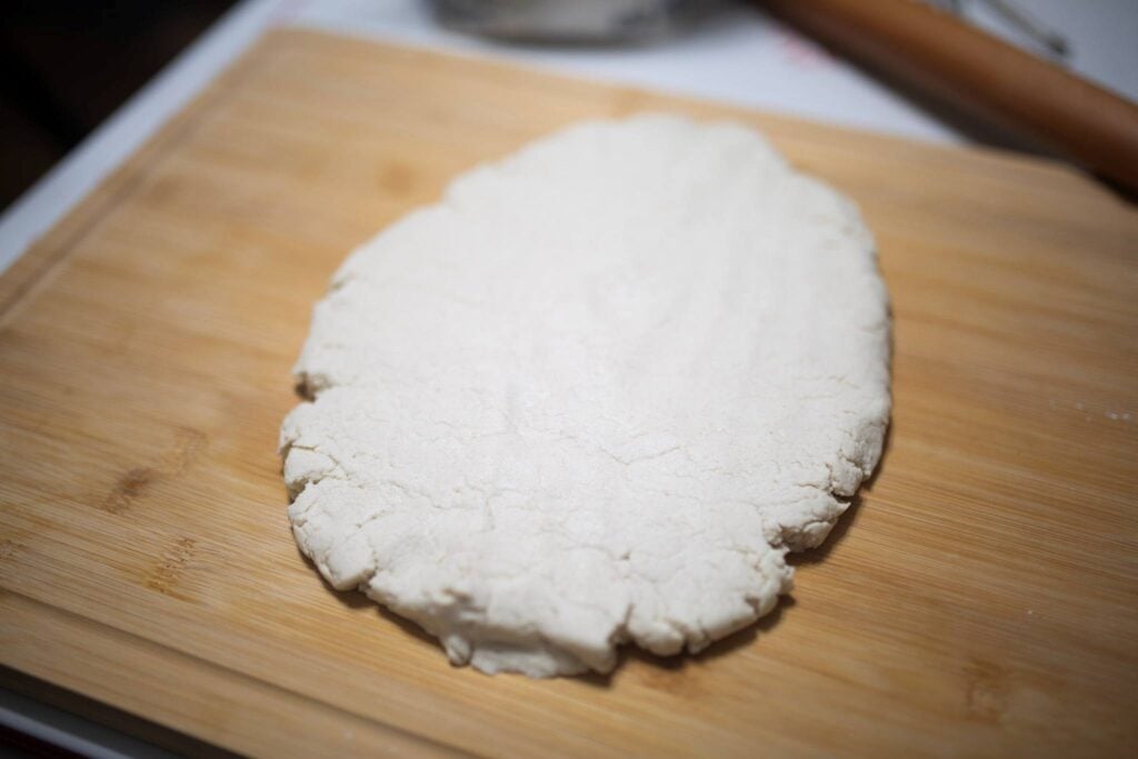 Biscuit dough is spread out into a circle on a wooden cutting board.