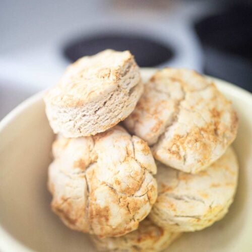 A cream colored bowl full of biscuits.