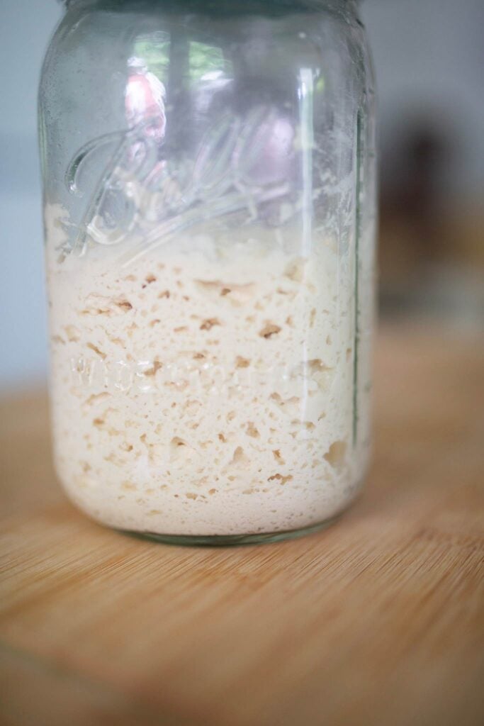 Sourdough starter in mason jar that is very bubbly sitting on a wood board.