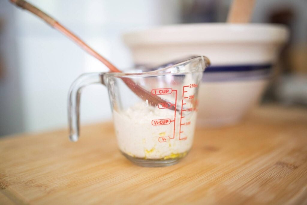 a glass measuring cup with sourdough starter and a wooden spoon in it.