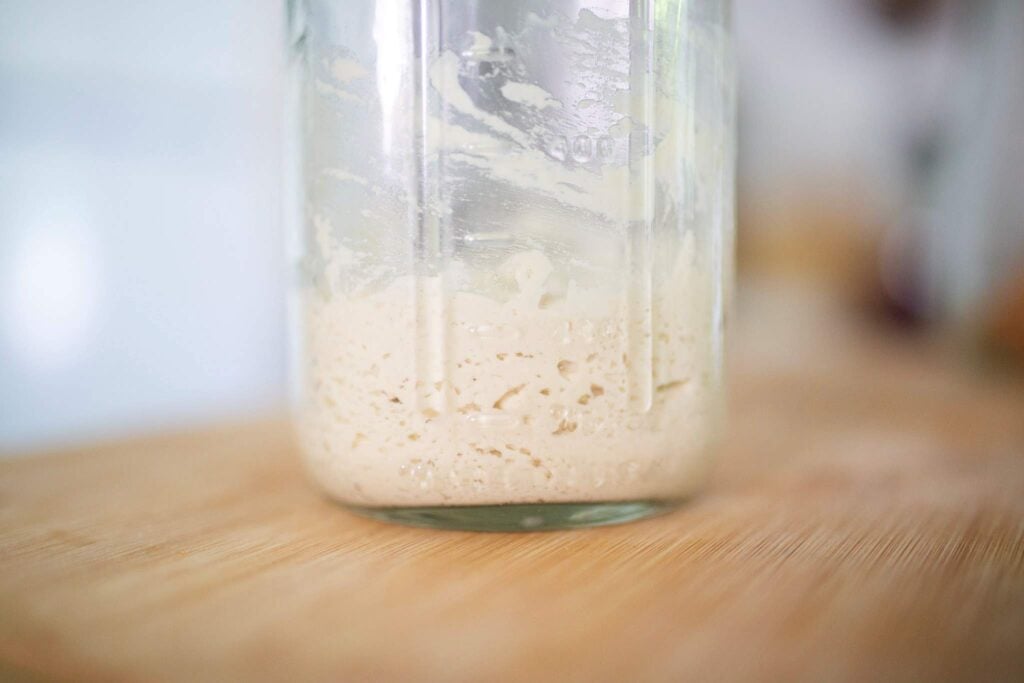 A jar of sourdough starter with a few bubbles in the bottom.