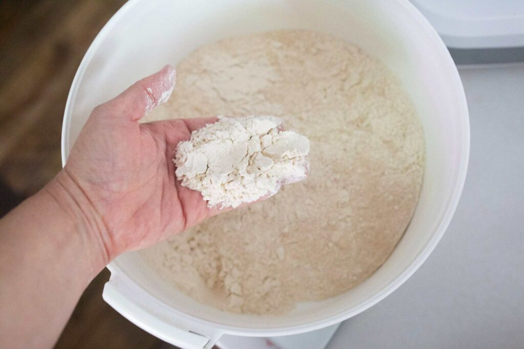 A hand is holding flour over a big white bowl of flour.