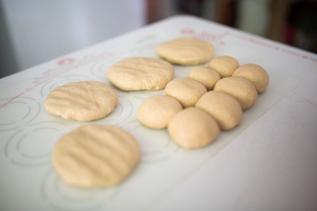 Dough shaped into rolls and hamburger buns on a silicone mat.