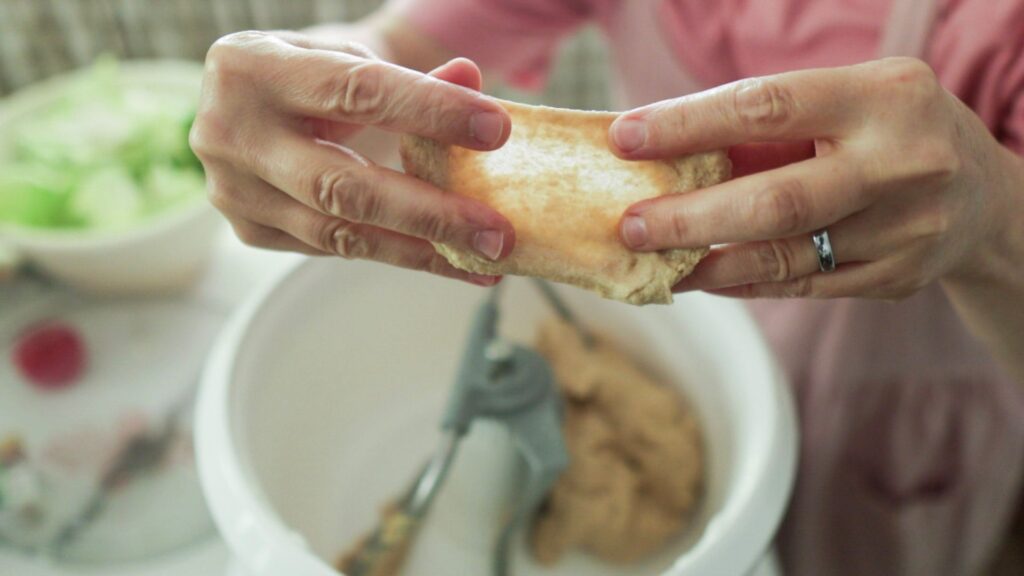 There are 2 hands stretching dough thin enough to see through it.