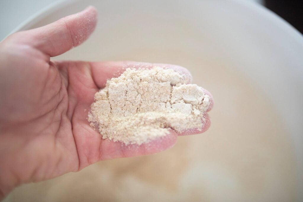 A hand is holding flour over a bin of flour.
