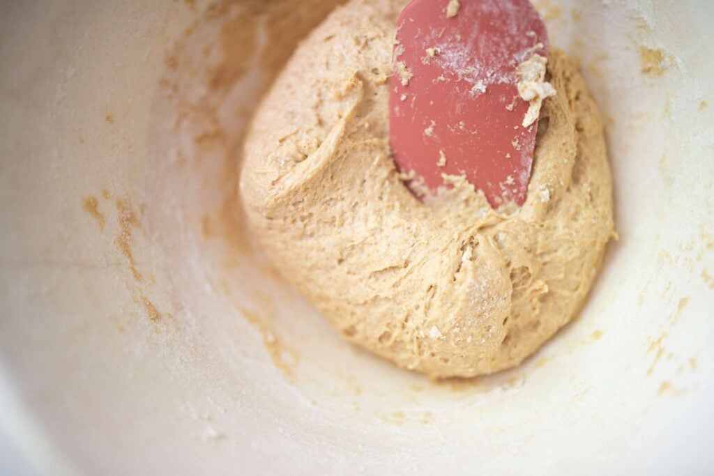 There is a dough ball with a rose colored spatula pulling it back to show the wet texture.