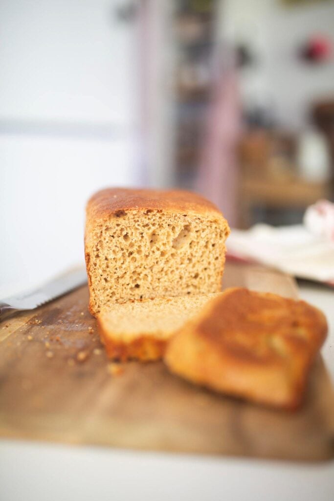 A loaf of bread on a wooden cutting board with 2 slices out in front.