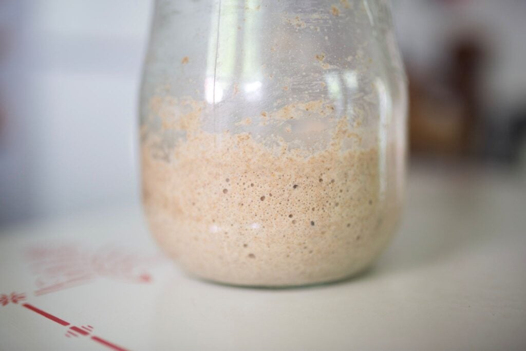 Bubbly sourdough starter in a glass jar sitting on a white and red table top.