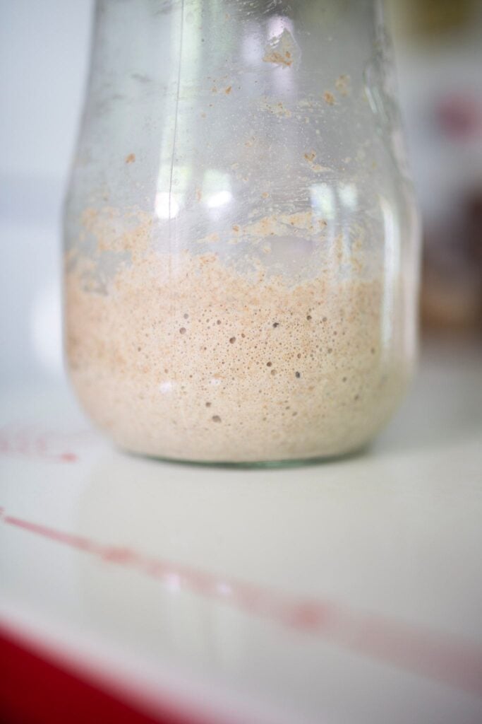 Bubbly sourdough starter in a glass jar on a white table.